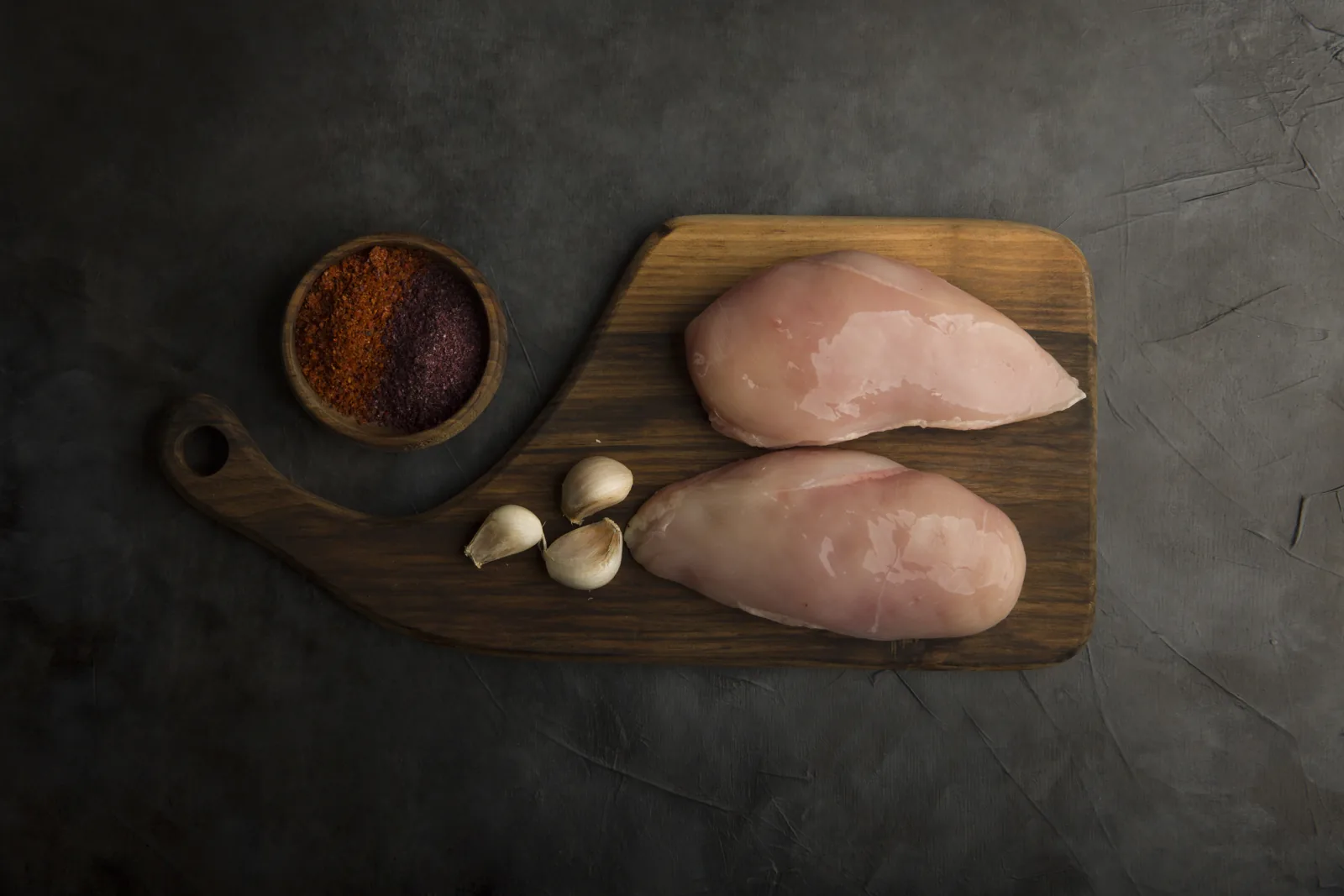 Pechugas de pollo crudas sobre tabla de madera con ajo y especias